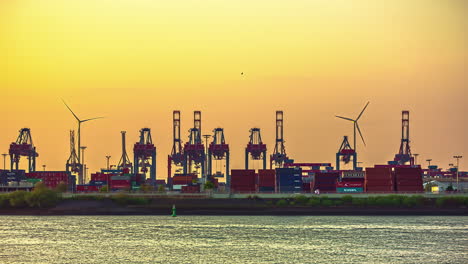 sunset over a shipping yard with wind turbines in the background - time lapse