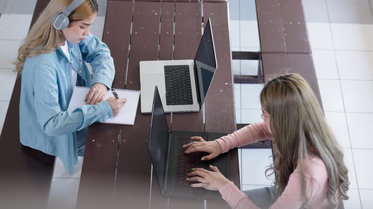 Two Asian girls student partners are working on a laptop help study together
