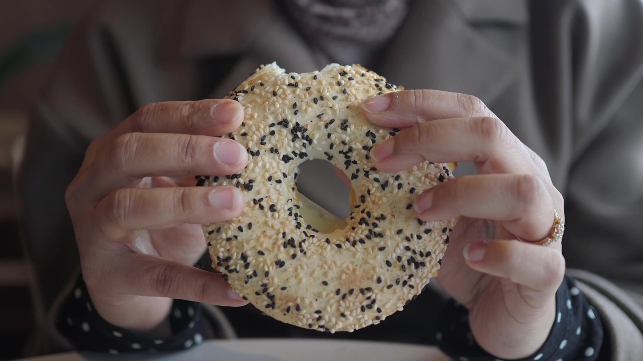 Close-up of Hands Holding and Eating a Sesame Bagel