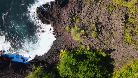 una cautivadora toma de avión no tripulado de arriba hacia abajo que ofrece una vista impresionante de una playa con poderosas olas azules que chocan energéticamente contra la orilla