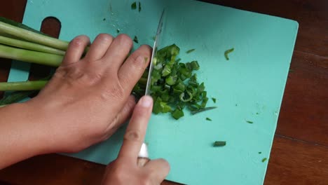 top view of women's hands cut green onions with a knife on a board