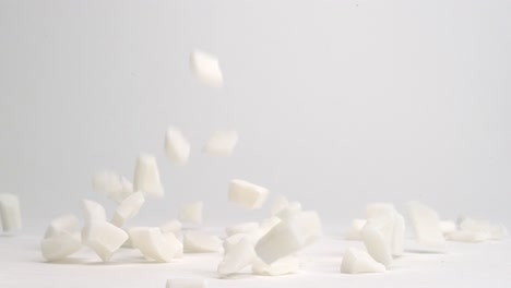 cubed white coconut chunks falling and bouncing onto white table top into pile in slow motion