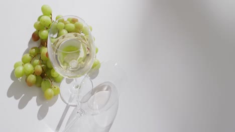 vaso de vino blanco y uvas sobre una superficie blanca con espacio para copiar