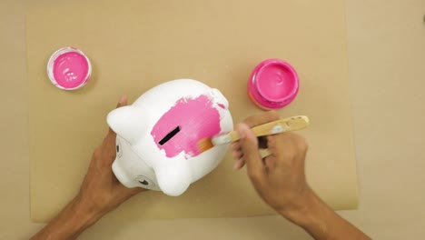 Weißes-Keramik-Sparschwein-Rosa-Mit-Pinsel-Auf-Braunem-Papier-Malen