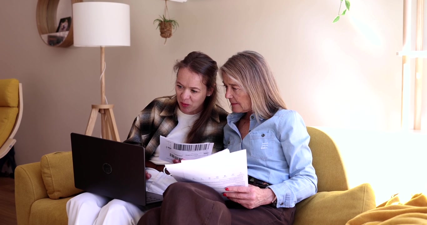 Due donne che esaminano documenti e usano un laptop su un divano