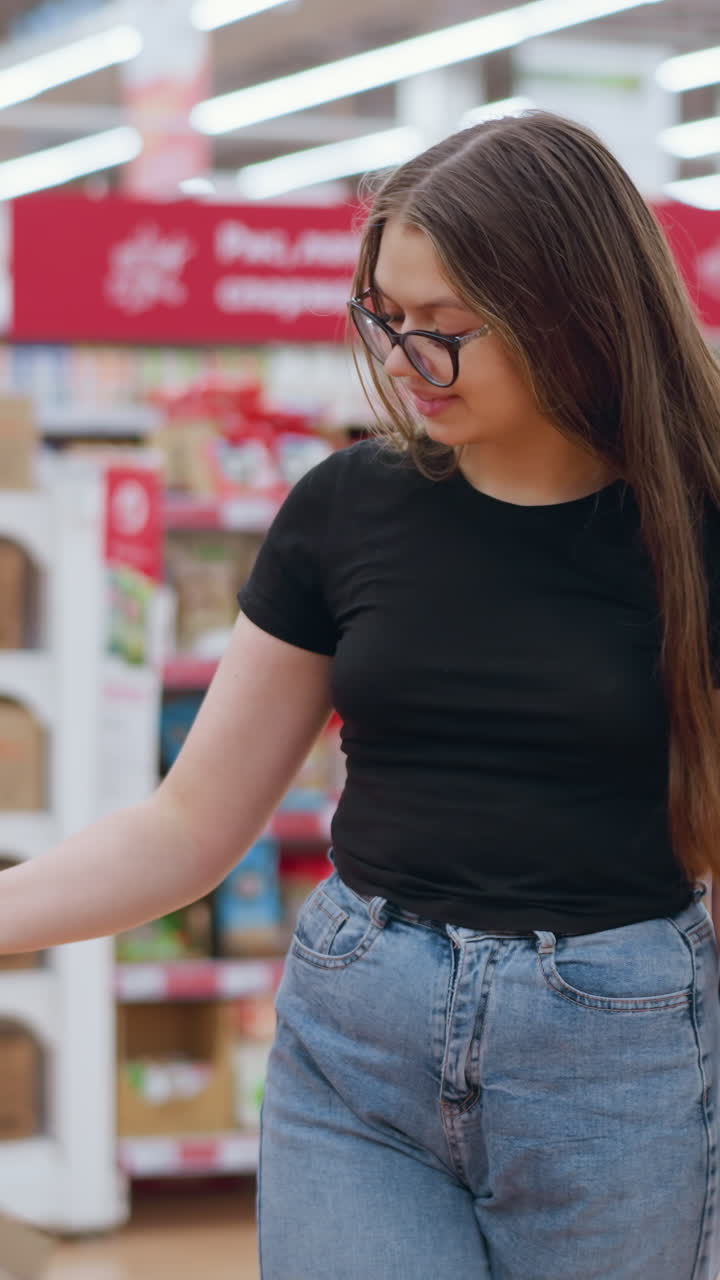 una mujer joven en la tienda de comestibles recoge una manzana roja de la exhibición, la observa y la deja caer, las etiquetas de precio y las señales son visibles en un entorno de tienda brillante y vibrante