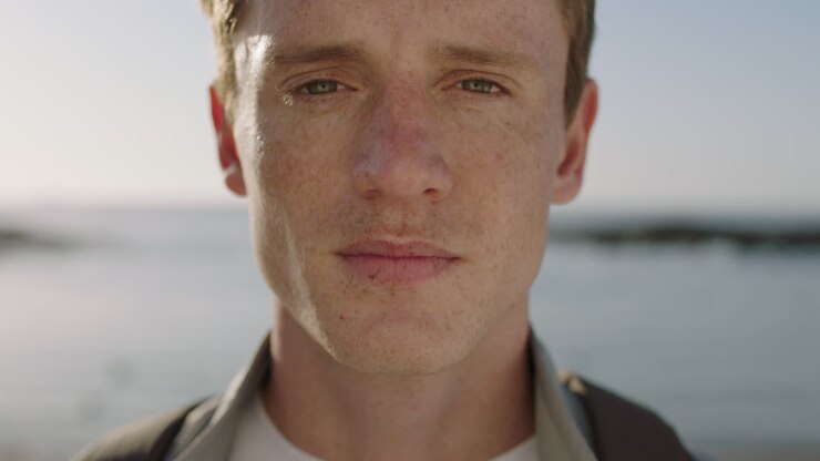 close up portrait of handsome young man looking thoughtful pensive on seaside background