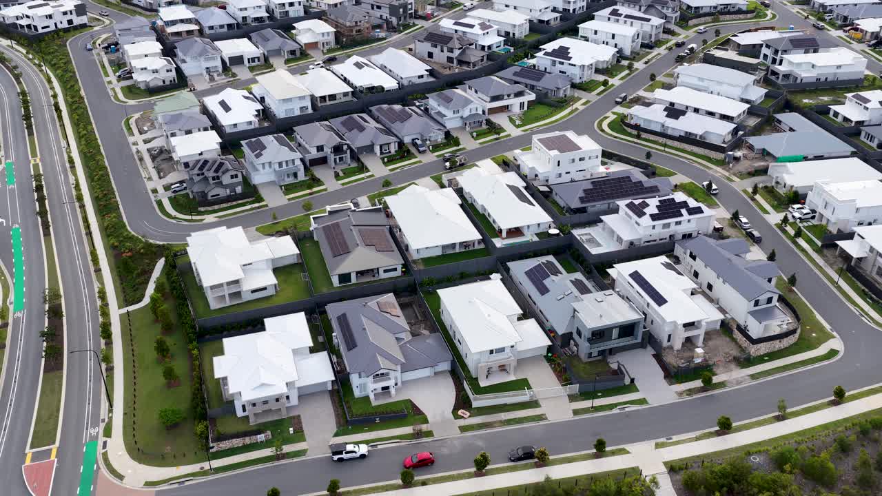 Drone glides over contemporary suburban homes, revealing winding streets, green spaces, and forested hills