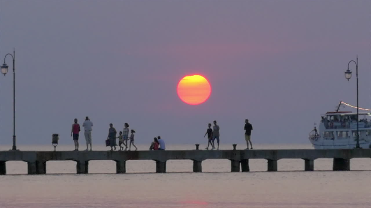 Ferry sailing by the pier with people at sunset
