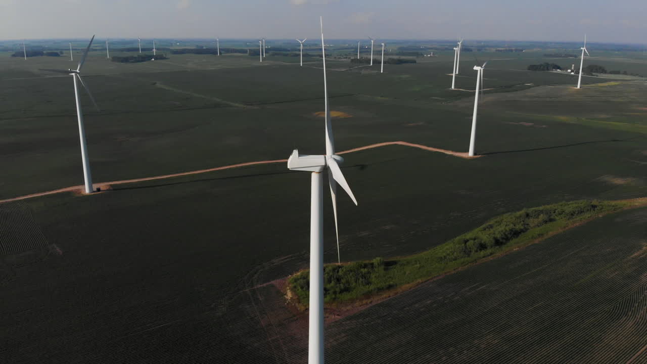 Drone orbiting around a windmill turbine in a green field of beans in the midwest