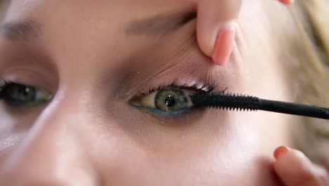 the make-up artist lifts the eyelid of the model and stains eyelashes with mascara stick. black colour. close up view