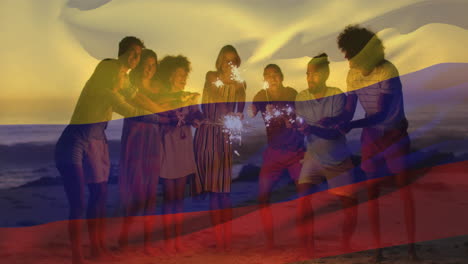 Animación-De-La-Bandera-Colombiana-Ondeando-Sobre-Diversos-Amigos-Con-Bengalas-Disfrutando-En-La-Playa.