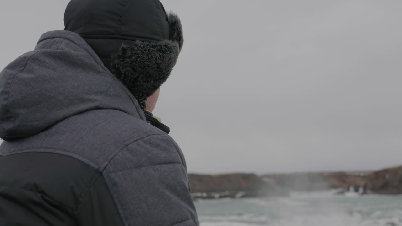 Approaching to Middle Age Man on Lookout Above Waterfall in Cold Winter Landscape of Iceland