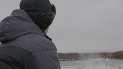 Acercándose-Al-Hombre-De-Mediana-Edad-Mirando-Por-Encima-De-La-Cascada-En-El-Frío-Paisaje-Invernal-De-Islandia