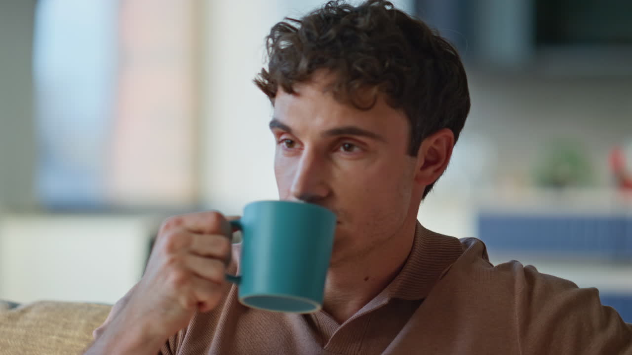 Thoughtful guy drinking coffee sitting sofa at relaxed home environment closeup