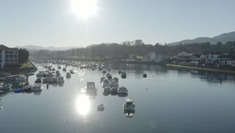 Bright sunny day at Saint-Jean-de-Luzover, Nivelle river, port and moored boats, sun reflects on water, La Rhune mountain in background, Basque Country in France. Aerial drone