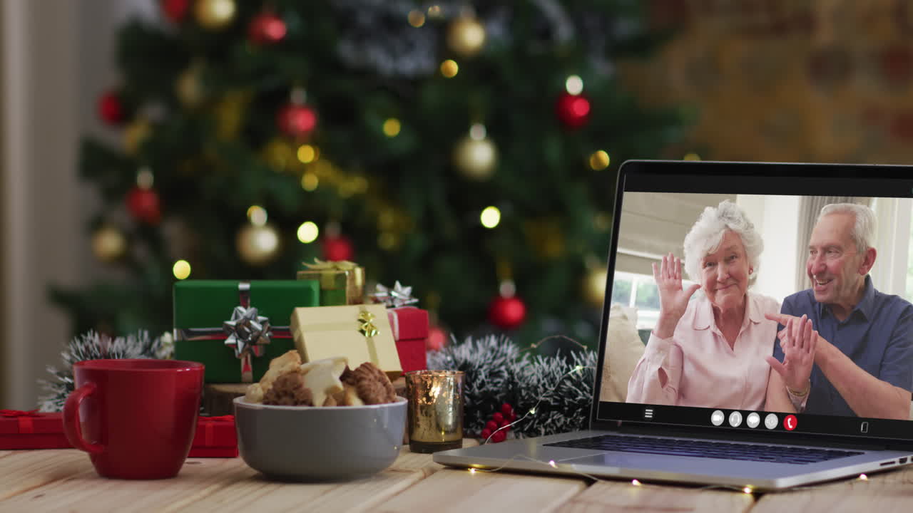una pareja de alto nivel caucásica saludando en una videollamada en una computadora portátil, con un árbol de navidad