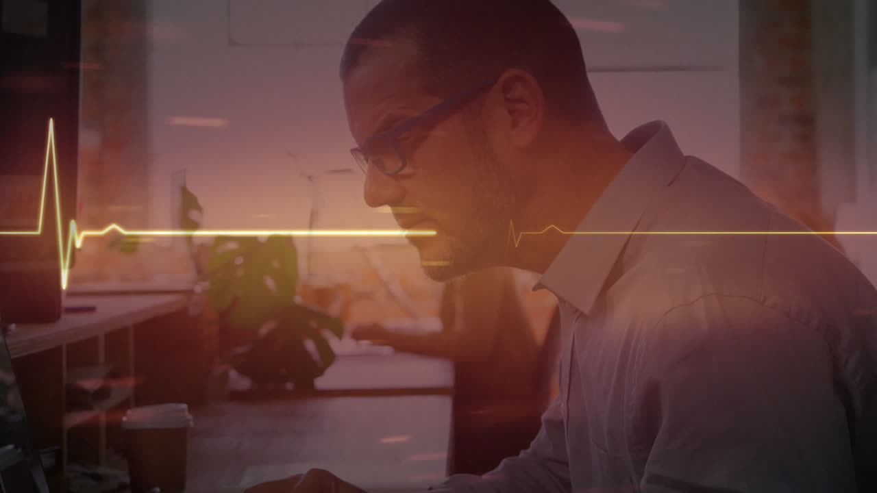 monitor de ritmo cardíaco rojo brillante contra hombre caucásico usando computadora en la oficina