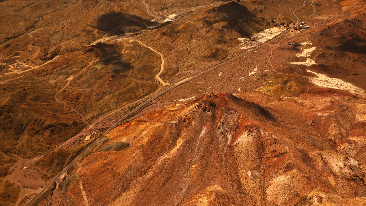 Flight above the lifeless arid landscape of Mojave desert. Long highway passes through the valley between the mountains. Aerial view.