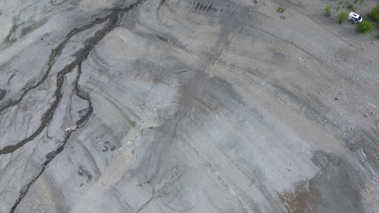 Jævn nedadgående 4K droneoptagelse, der viser en strand med en lille flod, omkringliggende træer og en campingvogn parkeret i nærheden. Optaget ved Lac de Serre Ponçon, de franske alper, maj 2025.