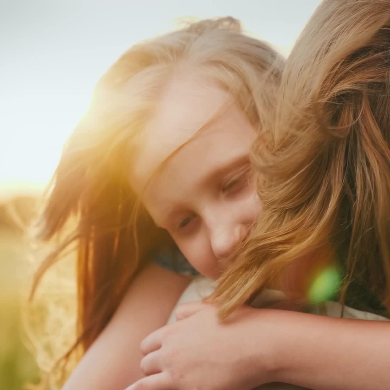 Una ragazza abbraccia sua madre sullo sfondo di un campo dove il vento fa ondeggiare il grano