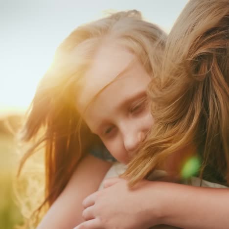 una niña abraza a su madre en el fondo de un campo donde el viento agita el trigo