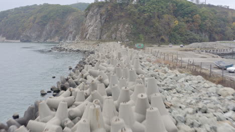 Volar-Sobre-Una-Línea-De-Rompeolas-De-Hormigón-Con-El-Muelle-En-El-Lado-Derecho-Y-Un-Acantilado-Boscoso-Empinado-En-El-Fondo