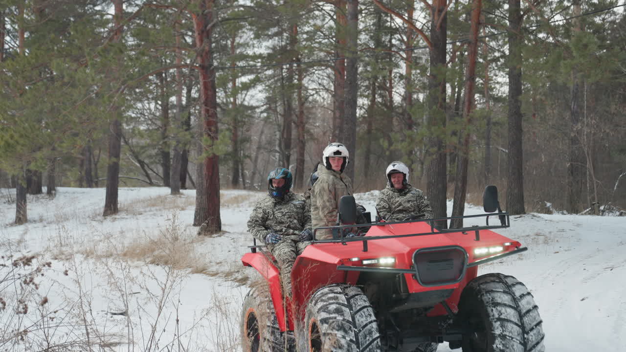 Tre piloti su un convoglio di ATV rossi in una pineta innevata, con giacche e caschi mimetici. I fari fendono la neve che cade, mostrando lavoro di squadra e risate mentre le ruote sollevano la neve in polvere, in una corsa coordinata.