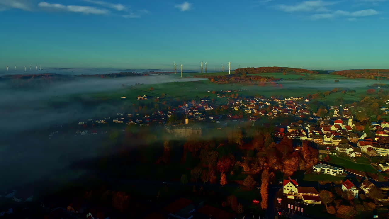 Aerial View of a Misty Village in Autumn with Wind Turbines