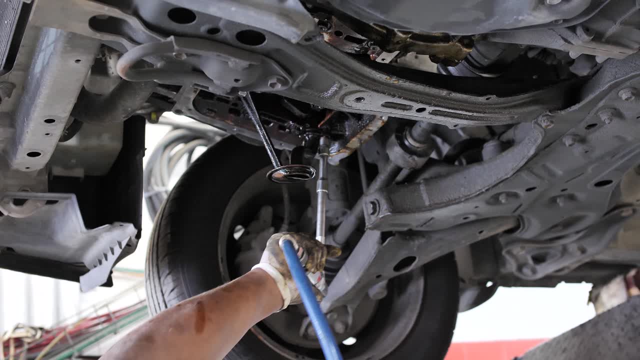 mecánico con llave neumática trabajando bajo chasis de camión, autoservicio, reparación