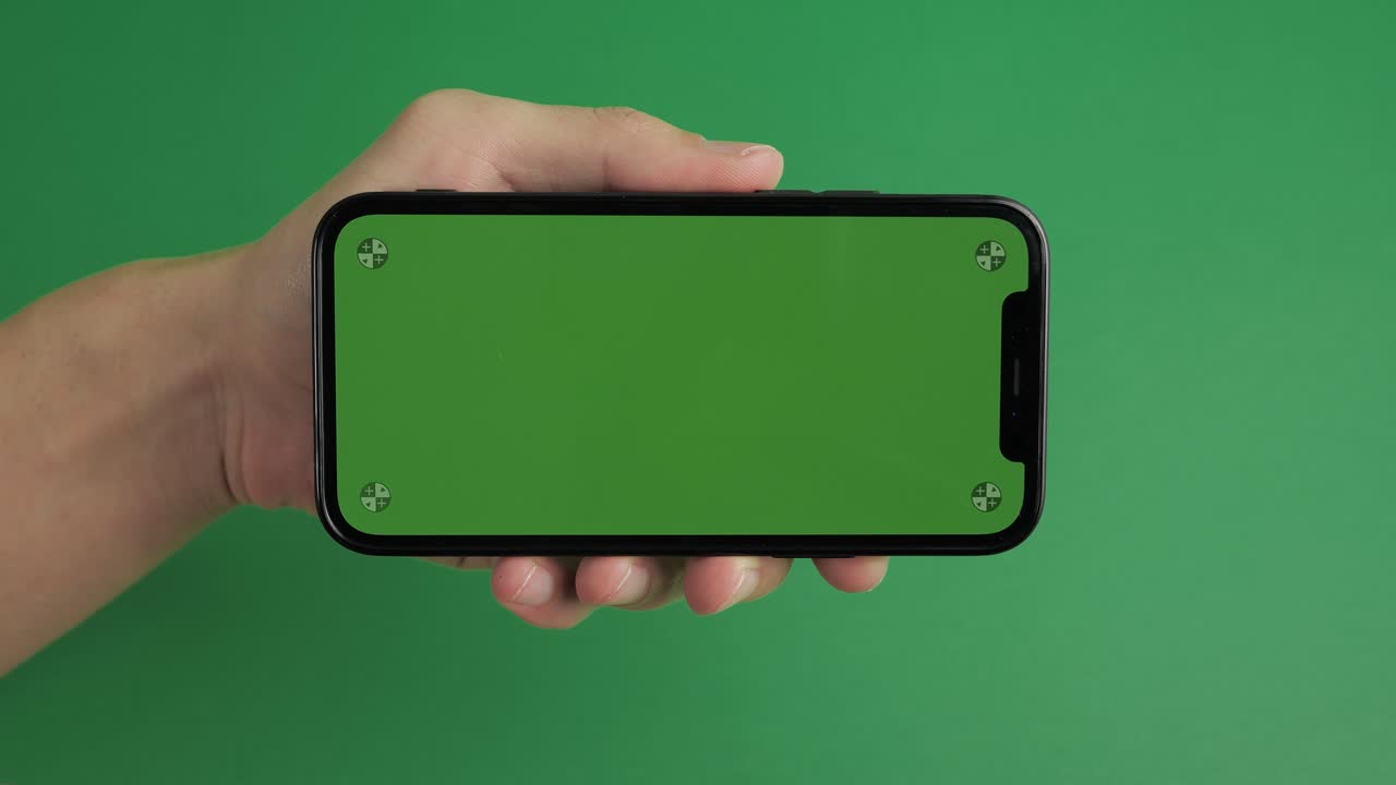 primer plano de mano masculina sosteniendo teléfono móvil con pantalla verde horizontal clave de croma tecnología de teléfono inteligente teléfono celular pantalla de mensaje táctil mano sobre fondo verde.