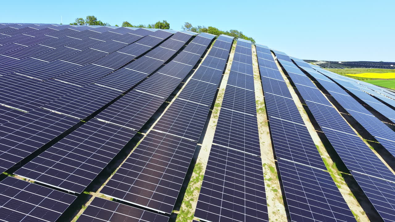 Pannelli solari coprono un grande campo sotto cieli sereni a mezzogiorno, mostrando la produzione di energia rinnovabile e la tecnologia in movimento