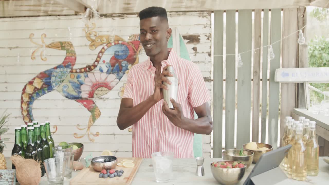 feliz barman afroamericano preparando cócteles detrás del mostrador en el bar de la playa, cámara lenta