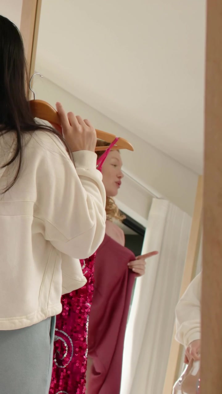 Vertikal video: Viser bøjler, kvinde i hættetrøje guider veninde, der prøver at smutte forbi et hjemmespejl, med plads til tekst.