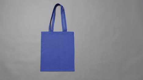 Close-up-of-blue-bag-on-grey-background,-with-copy-space,-slow-motion