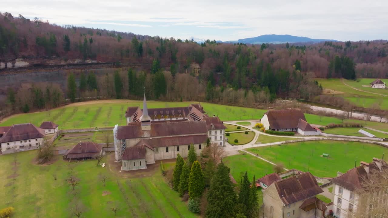 Elokuvamainen droonilento Abbaye d’Hauteriven yllä lähellä Fribourgia, esitellen historiallisen luostarin Sarine-joen ja rauhallisen sveitsiläisen maiseman ympäröimänä.