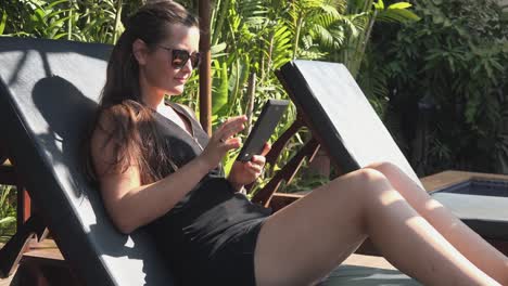 medium side shot of a young woman reading an e- book on a tablet by the pool