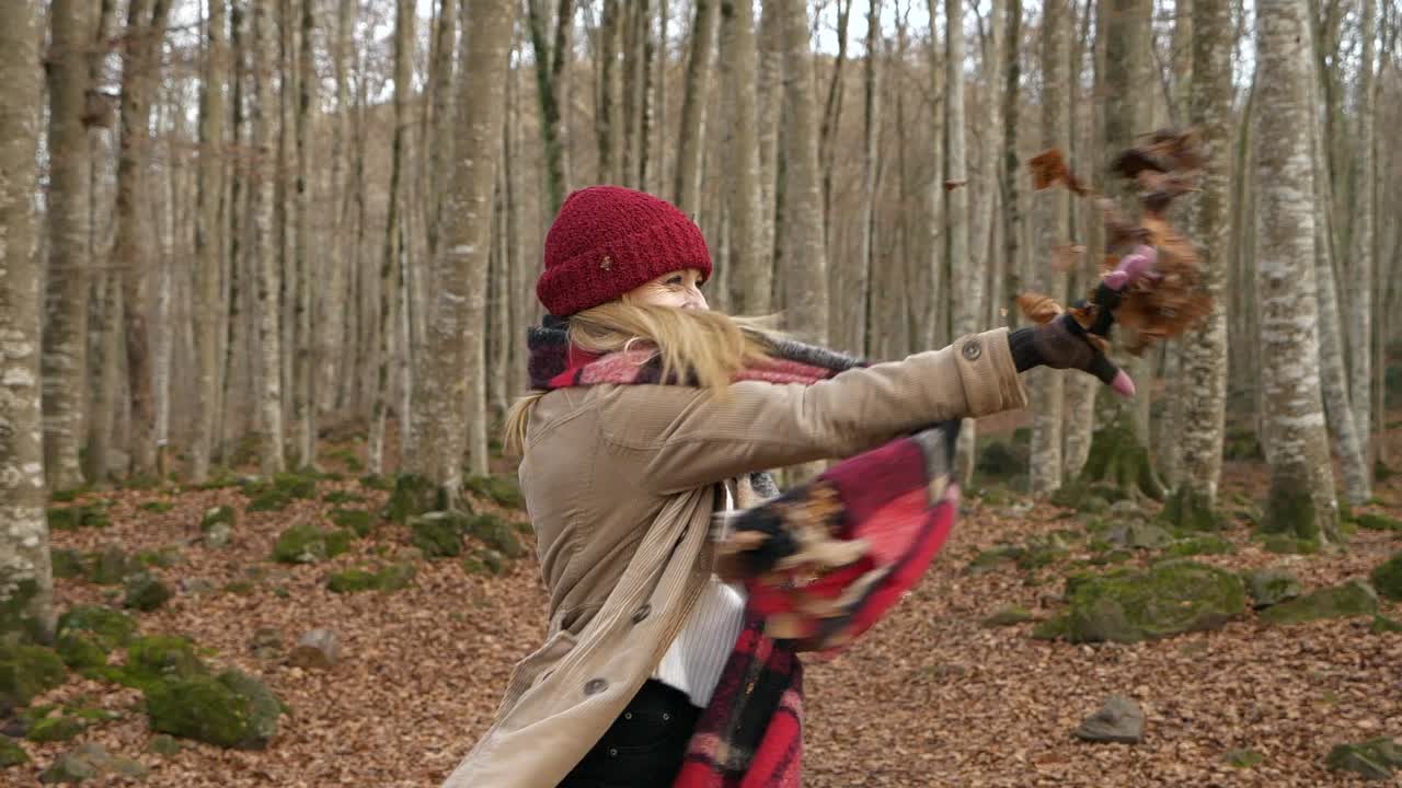 mujer joven sonríe y disfruta tirando hojas secas en el bosque