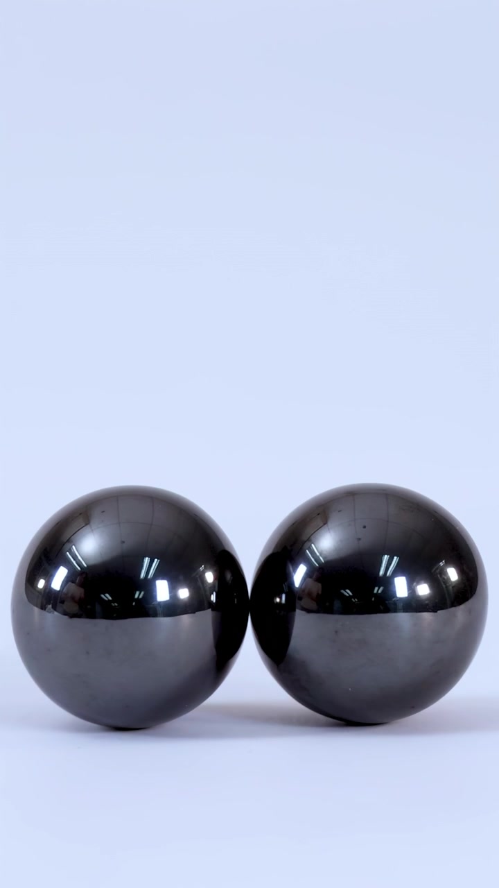 Close-up shot of two metallic magnetic balls rolling together and connecting on a plain background