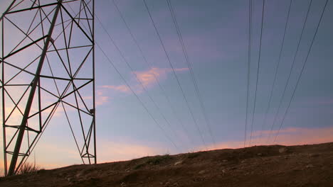 un ciclista de montaña masculino, realiza un truco de caballito, deslizándose debajo de una torre de línea eléctrica, mientras el sol bajo perfila su forma