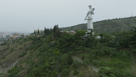 dolly in aerial shot of the kartlis deda monument and tbilisi cityscape