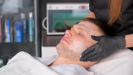 focused professional cosmetologist in glasses, wearing gloves, preparing for a lymphatic drainage facial massage in a well-lit spa room.