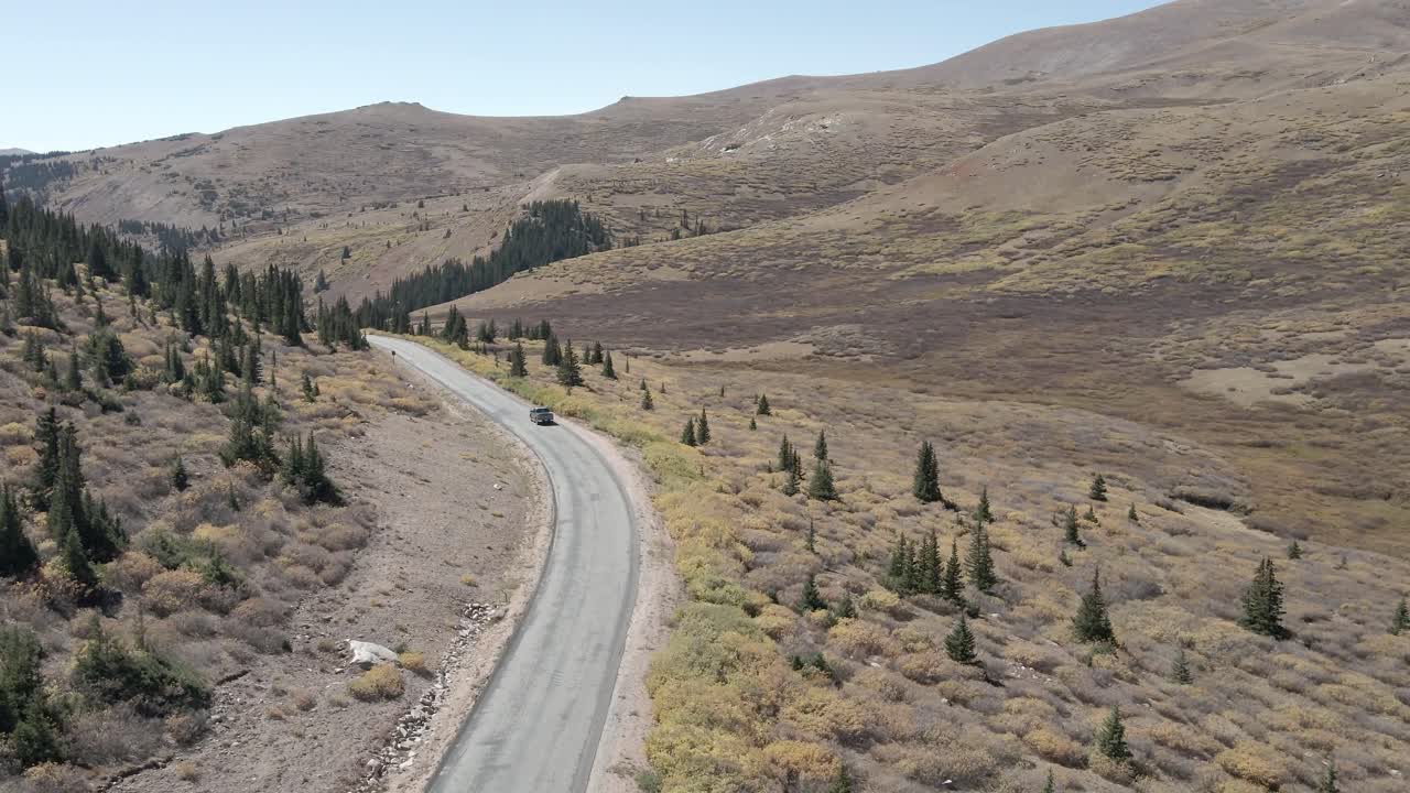 Aerial view of the Guanella Pass highway following a vehicle during the fall in Colorado. Filmed in the Rocky Mountains with a forward dolly movement.