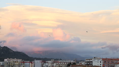 Hermosa-Vista-De-Ajaccio-Al-Atardecer,-Pájaros-Volando-En-El-Cielo-Con-Nubes-Coloridas