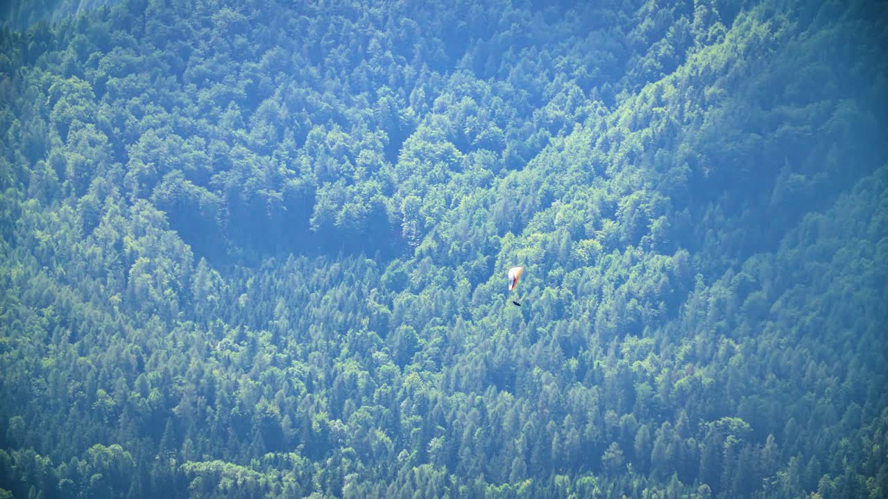 먼 거리에 있는 숲이 우거진 언덕에 대해 패러글라이딩하는 사람