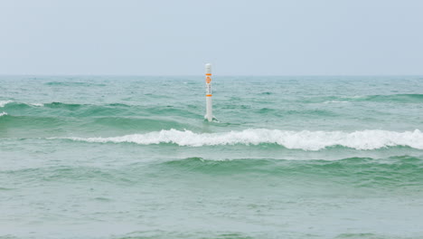 large waves rolling past a swim marker near a beach on lake michigan