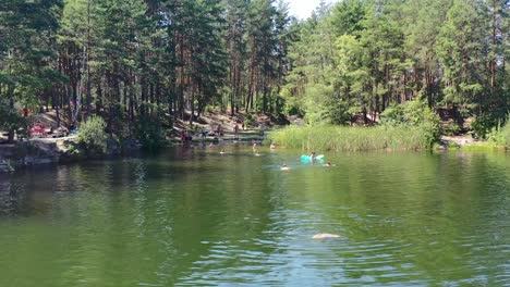 people swimming and relaxing in a beautiful lake surrounded by a forest