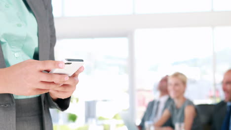 Businesswoman-texting-on-her-mobile-phone-with-colleague-in-background