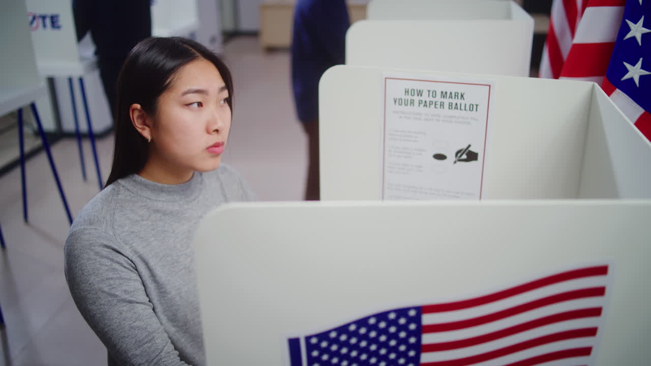 Asian Woman Looking at Camera Standing in Voting Booth Dolly Shot of Asian Woman Thinking and Choosing Presidential Candidate to Vote for in Voting Booth at Polling Station Looking at Camera American Citizen during National Election Day in the Usa