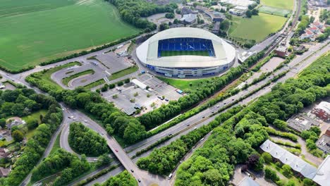 slow aerial drift reveals brighton’s stadium nestled below, cradled by a web of trains and a humming motorway. a serene approach to a pulse of energy.